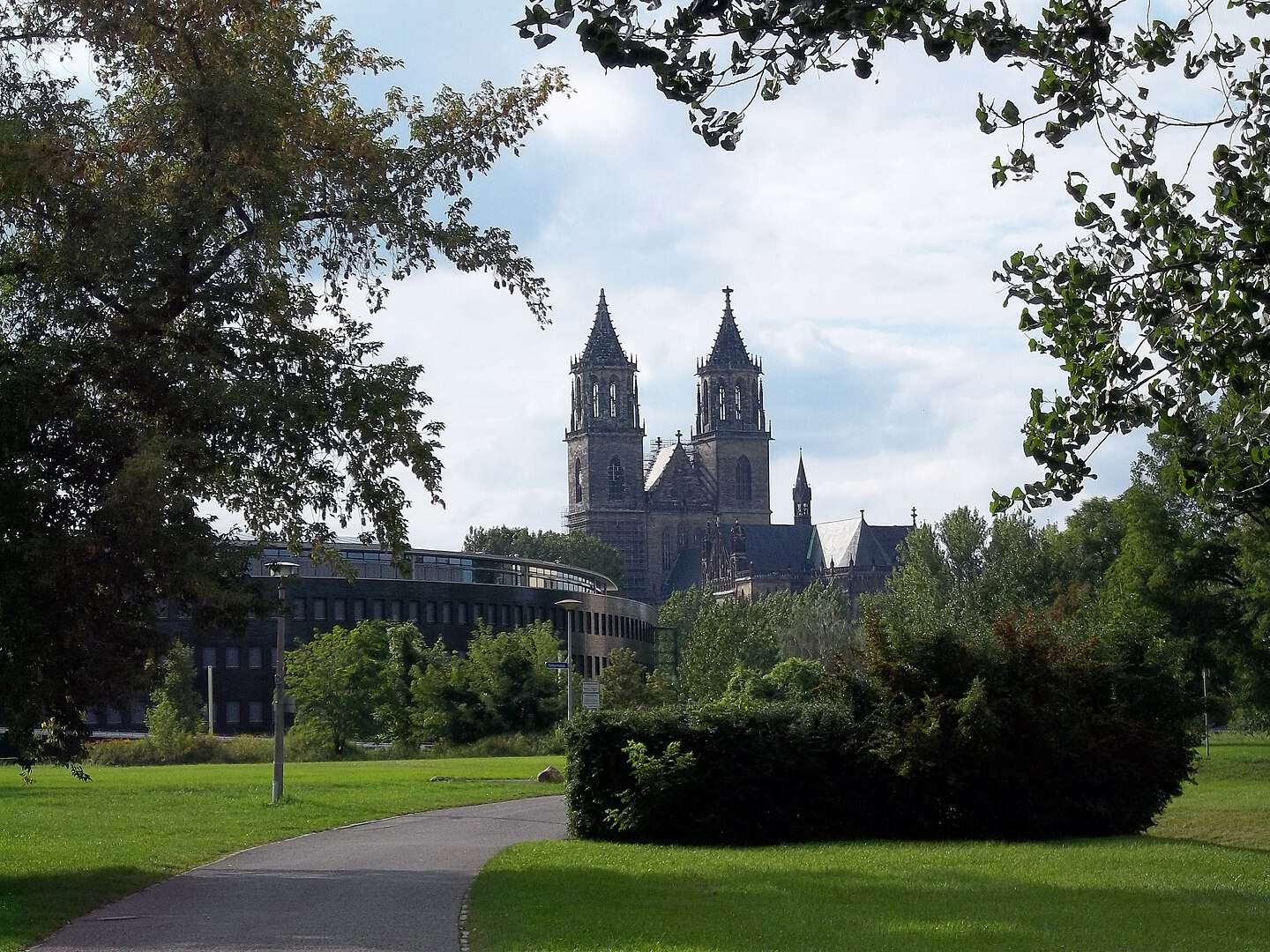 Ein grüner Park mit Weg und Bäumen vor einer historischen Kirche in Magdeburg.