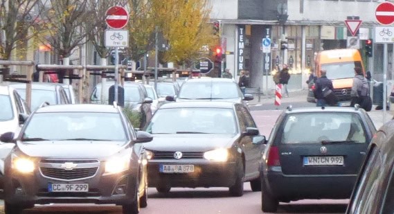 Stau auf einer Stadtstraße mit mehreren Autos, Verkehrszeichen sichtbar.