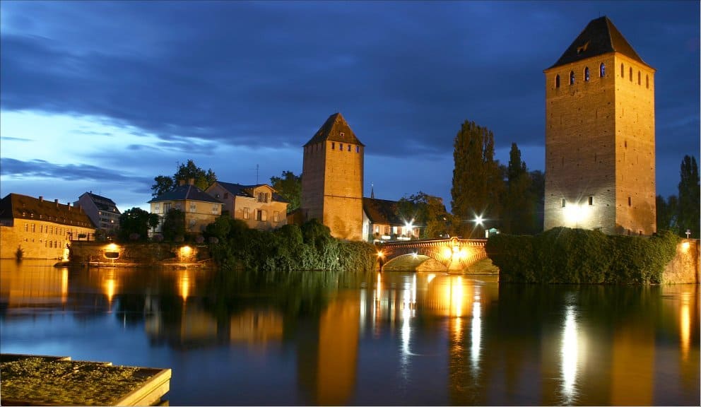 Hochwasserstand der mittelalterlichen Stadtmauer bei Nacht, beleuchtet und reflektiert im Fluss.