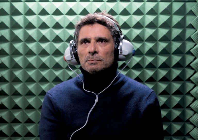 Ein Mann trägt Kopfhörer vor einer schallabsorbierenden Wand, symbolisiert akustische Wahrnehmung.