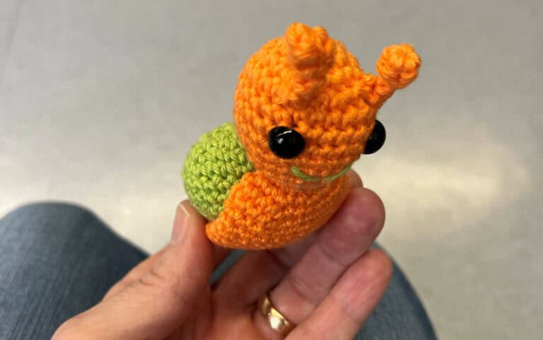 Schnecke aus gestricktem Garn, handgefertigt, mit schwarzen Augen und grüner Spirale am Rücken.