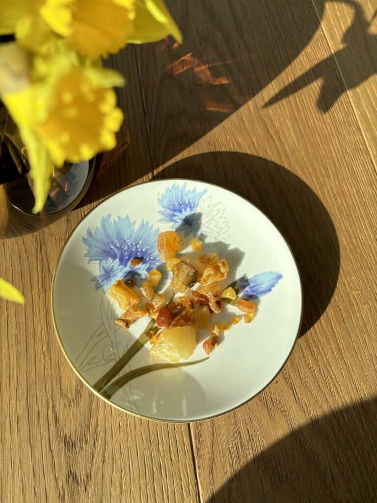 Früchte und Honig auf einem blumigen Teller bei Sonnenlicht.