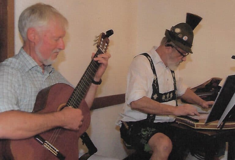 Zither-Spieler und Gitarrist bei einem Musikauftritt in einem Raum.