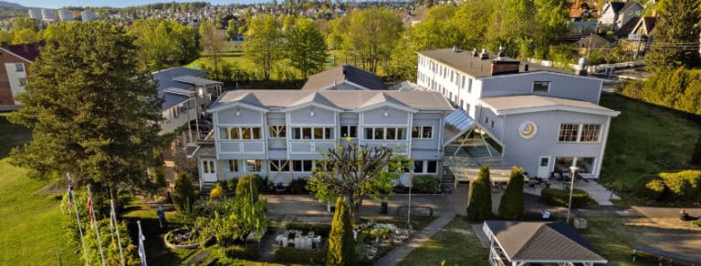 Modernes Tagungshaus in Oslo für Schwerhörigenseelsorge, umgeben von Natur und Bäumen.