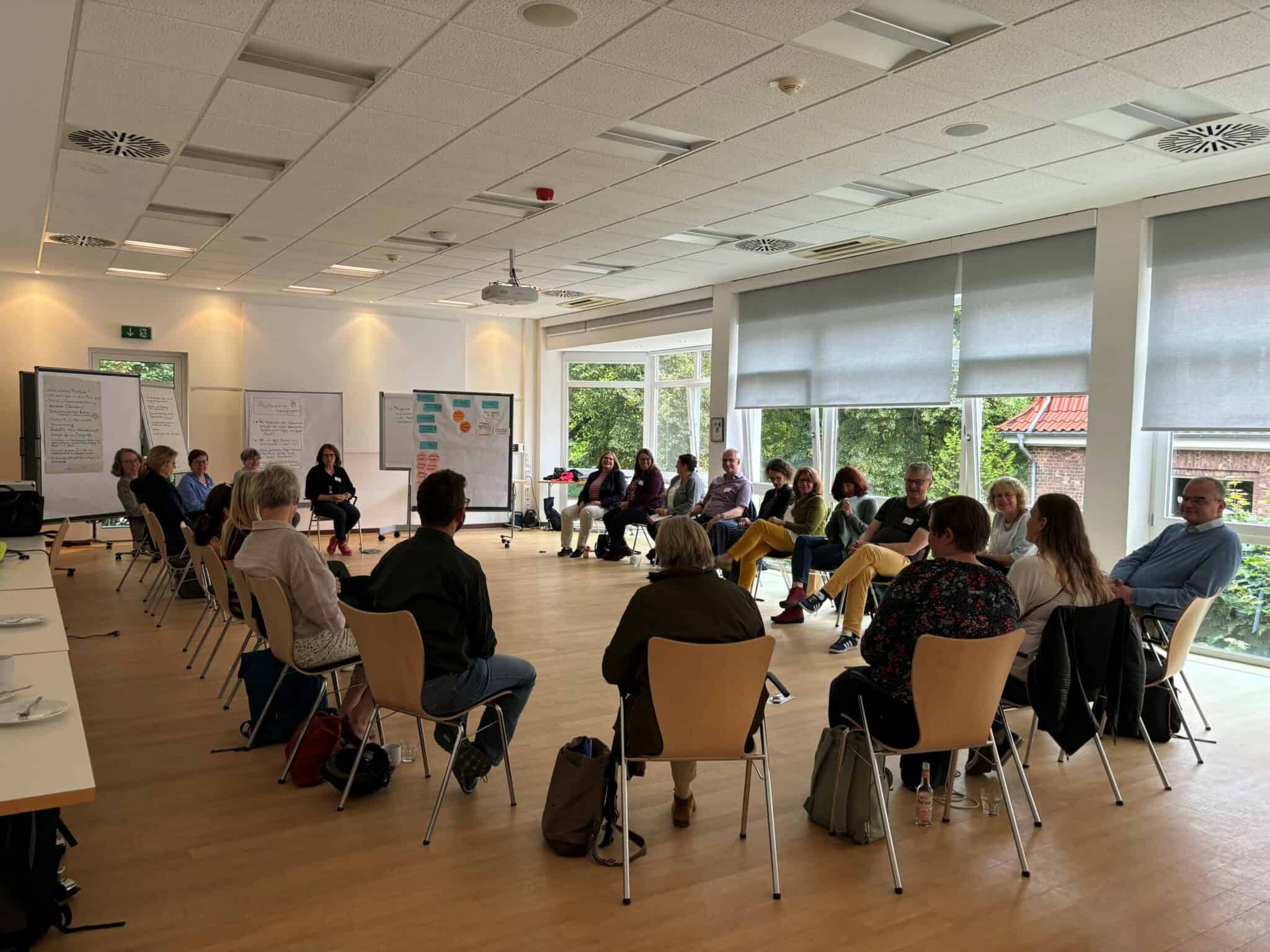 Menschen in einem Workshop oder Seminar sitzen in einem großen, hellen Raum in einem Kreis.
