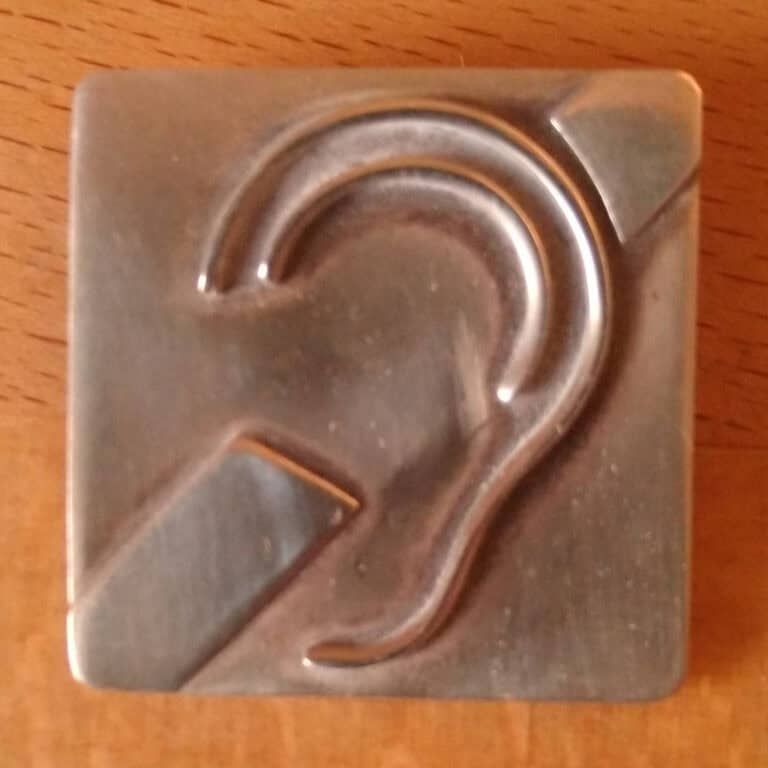 Silbergraue Brosche in Form eines Ohres auf Holzuntergrund.