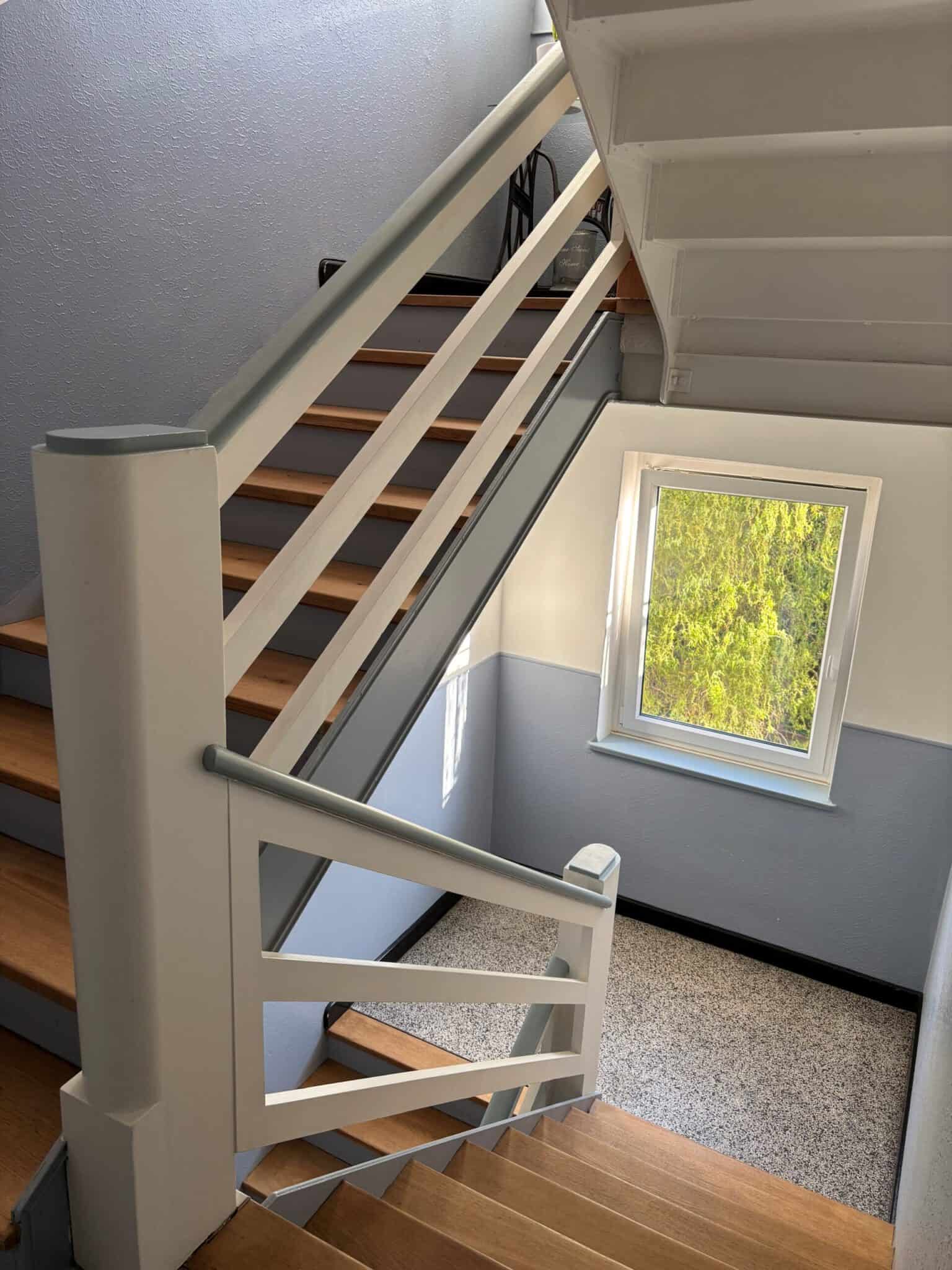 Treppenhaus mit Holzstufen und weißem Geländer, Blick nach oben zur oberen Etage.