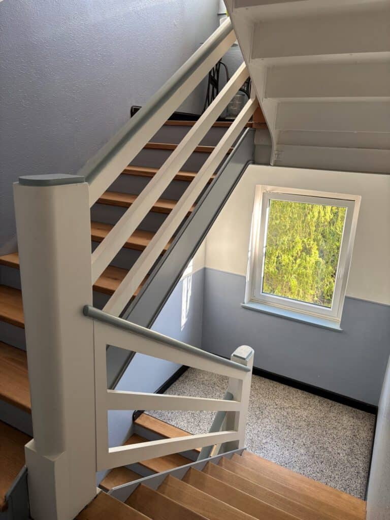 Treppenhaus mit Holzstufen und weißem Geländer, Blick nach oben zur oberen Etage.