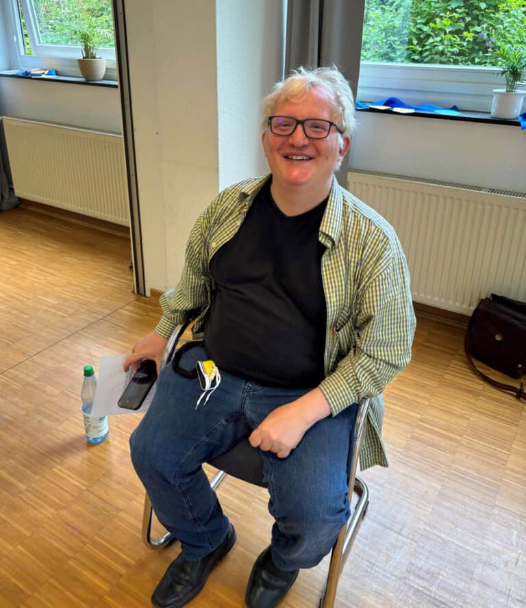 Fröhlicher schwerhöriger Mann im Rollstuhl in einem hellen Raum.