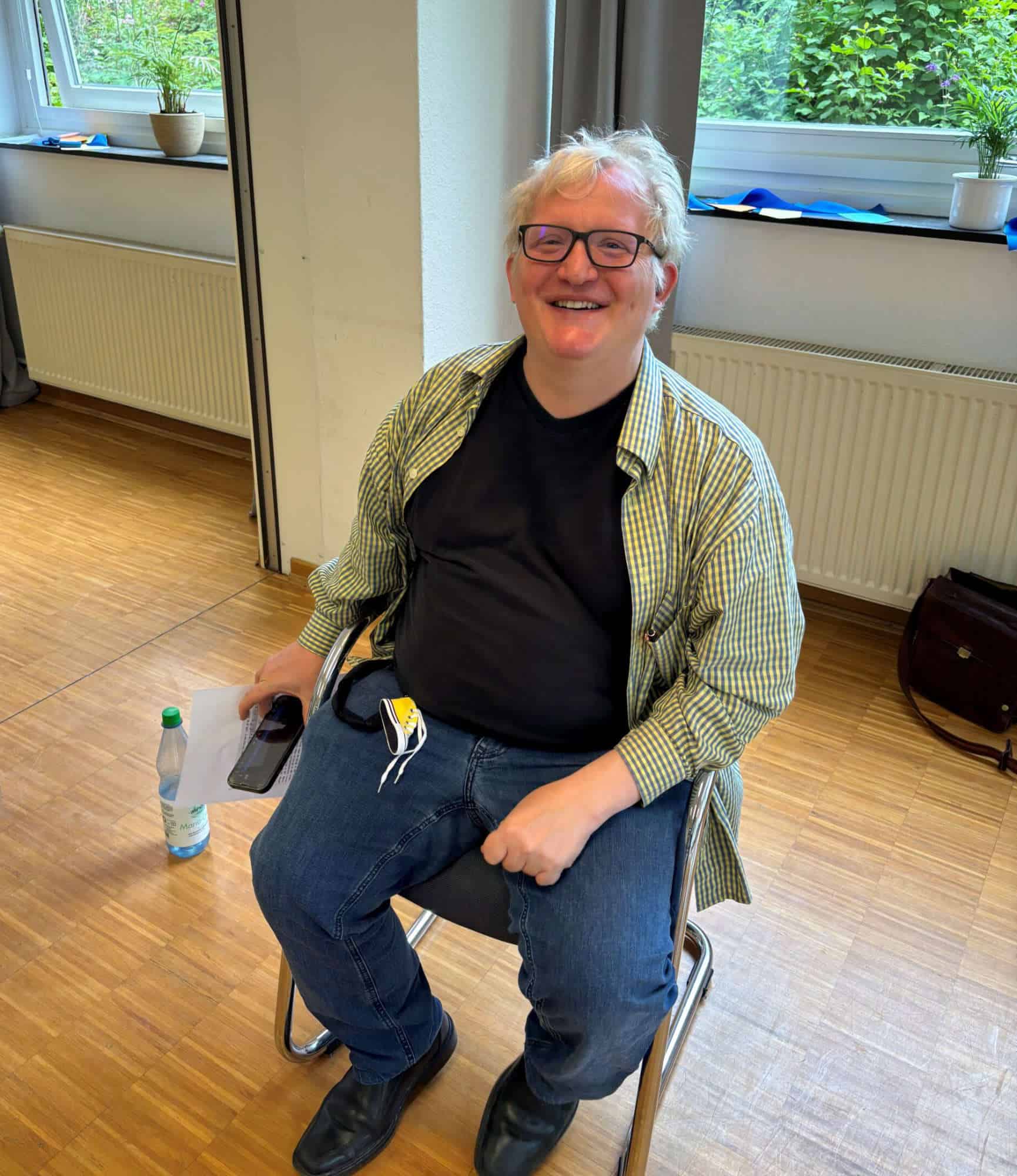 Fröhlicher schwerhöriger Mann im Rollstuhl in einem hellen Raum.