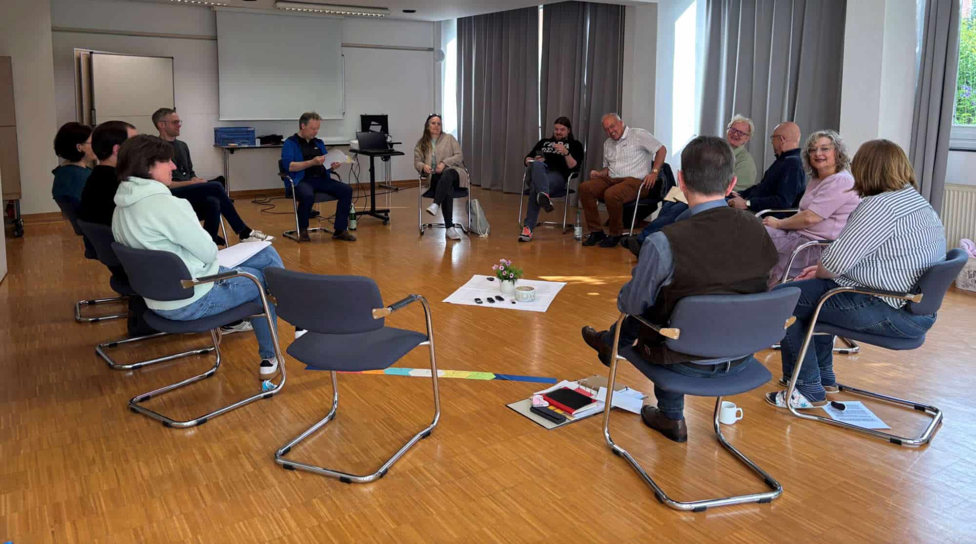 Gruppe von Menschen in einem Kreis bei einer Diskussion im Raum.