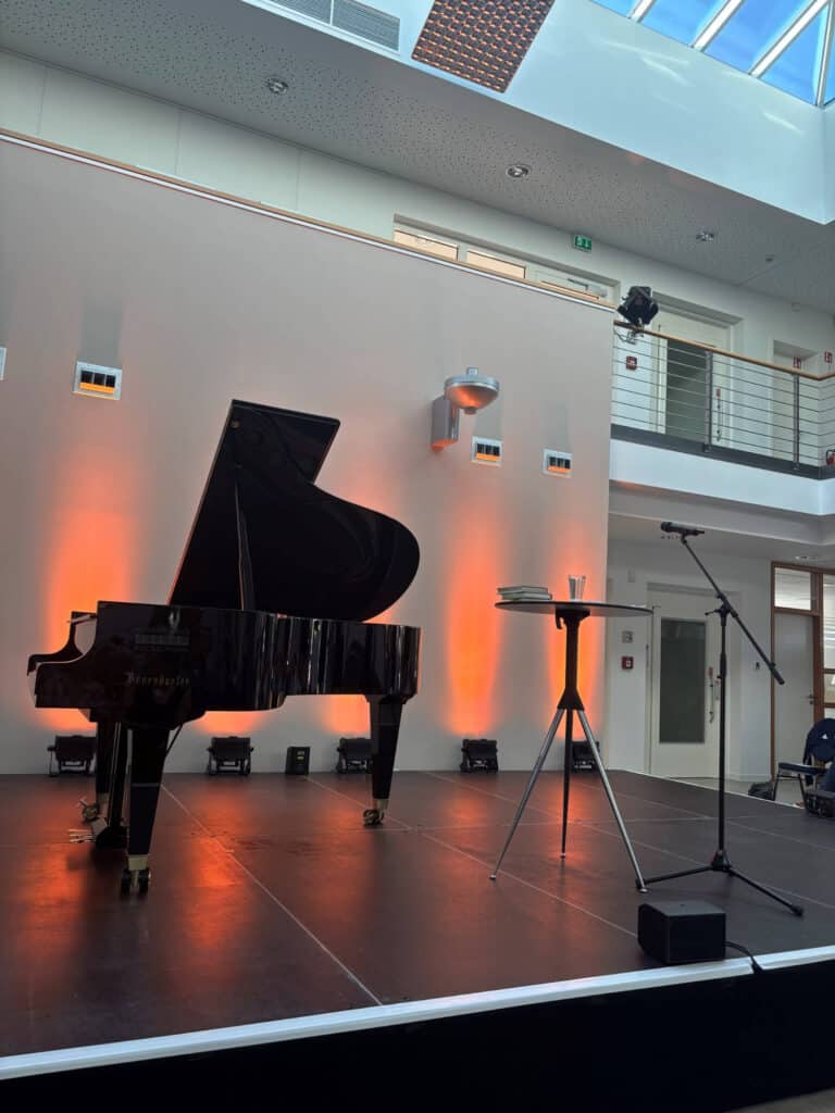 Ein Flügel auf einer Bühne mit Mikrofon und Beleuchtung im Hintergrund.