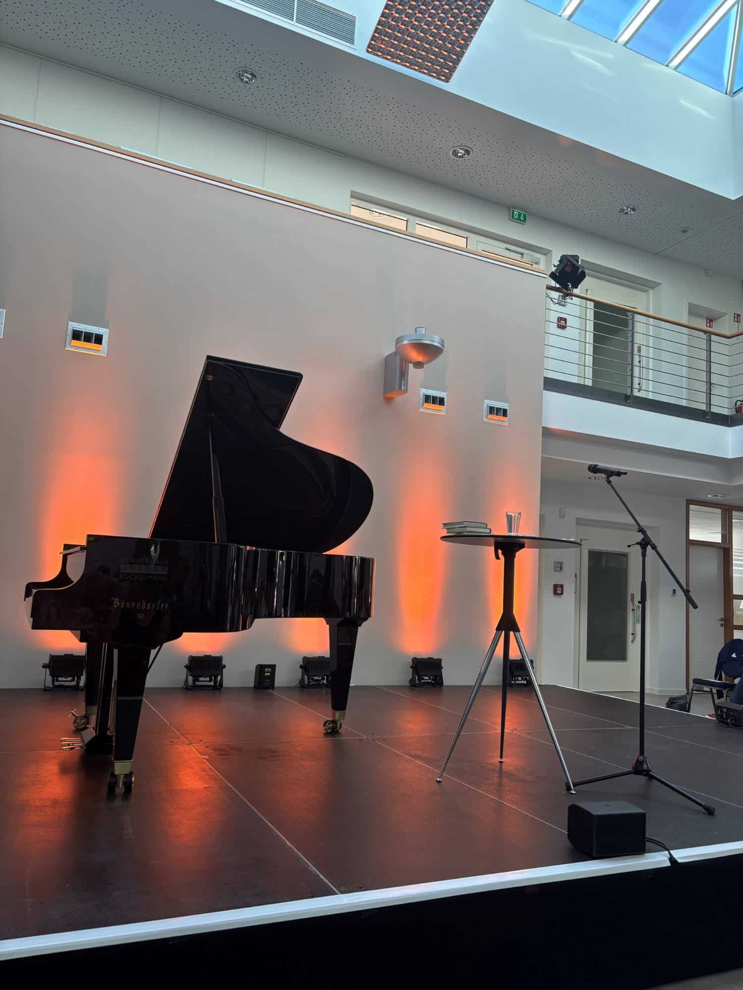 Ein Flügel auf einer Bühne mit Mikrofon und Beleuchtung im Hintergrund.