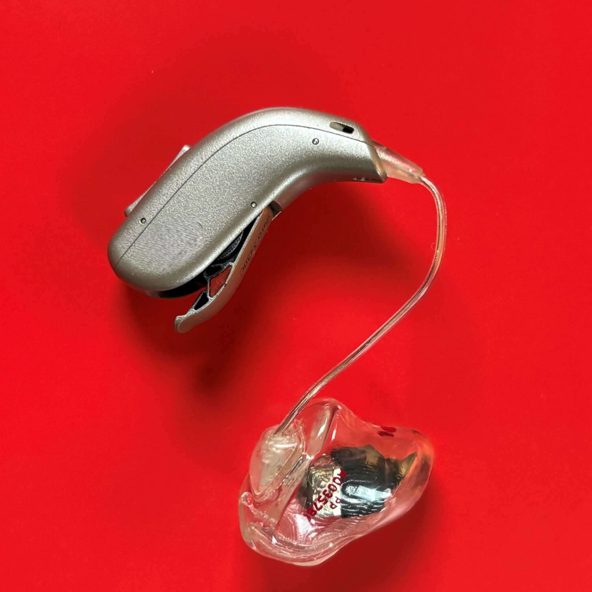 Gehörgerät mit rotem Hintergrund, symbolisiert Unterstützung für Schwerhörige in Kirche und Diakonie.