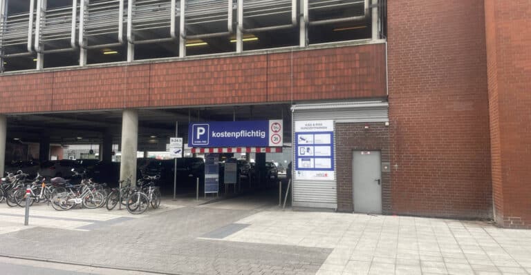 Parkhaus mit kostenpflichtigem Parkschein und Fahrradständern vor einem roten Backstein-Gebäude.