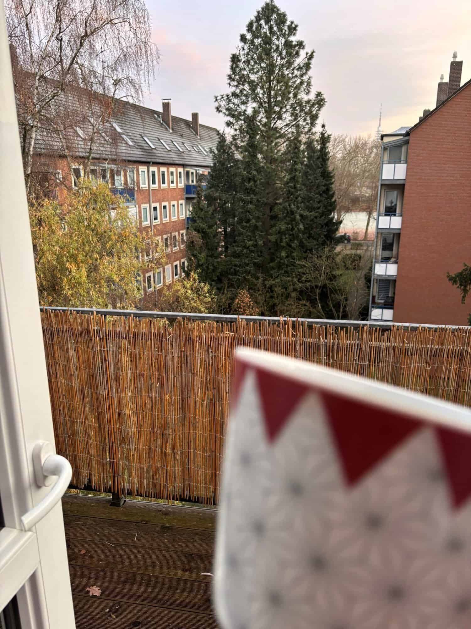 Balkon mit Blick auf Bäume und Wohnhäuser bei Sonnenaufgang in einer urbanen Umgebung.