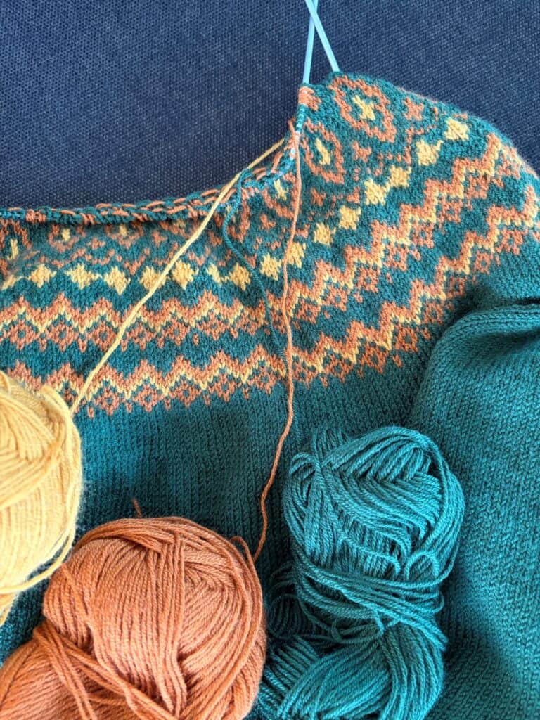 Strickwaren und Wolle in bunten Farben, mit Stricknadeln und einem halbfertigen Strickstück.