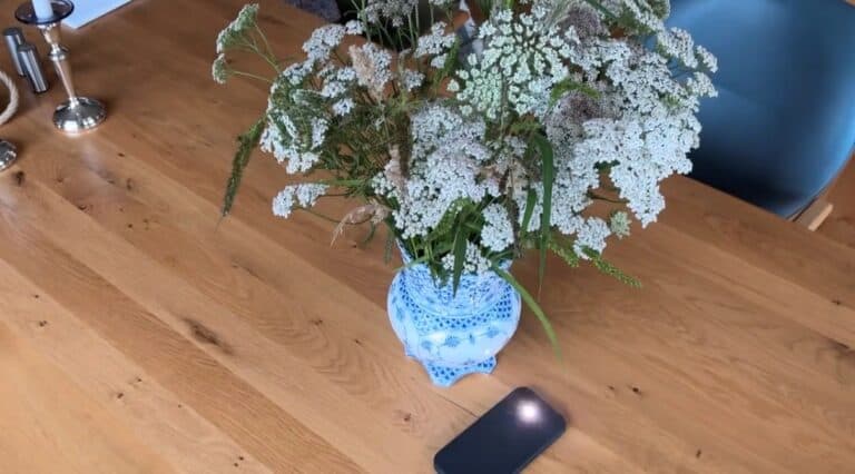 Blumenstrauß in blauer Vase auf Holztisch neben Smartphone.